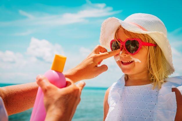 little girl wearing hat, sunglasses, and sunscreen on the beach | Ward Realty