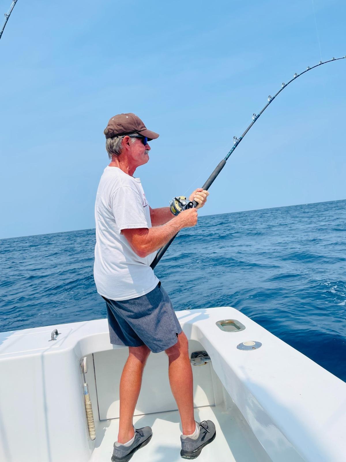 man reeling in shark on fishing charter boat | Ward Realty